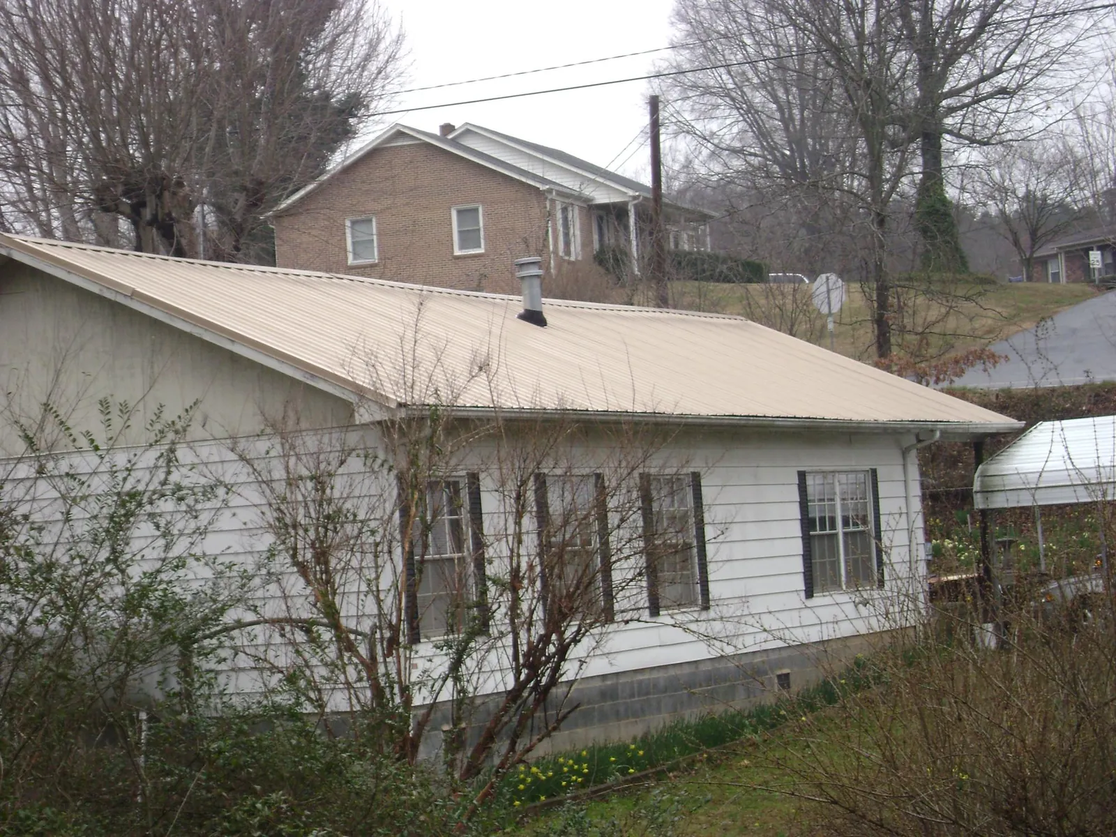 Tan metal roof on a white sided house set into a hillside — Commercial Roofing by Roofing Brothers in Murdock
