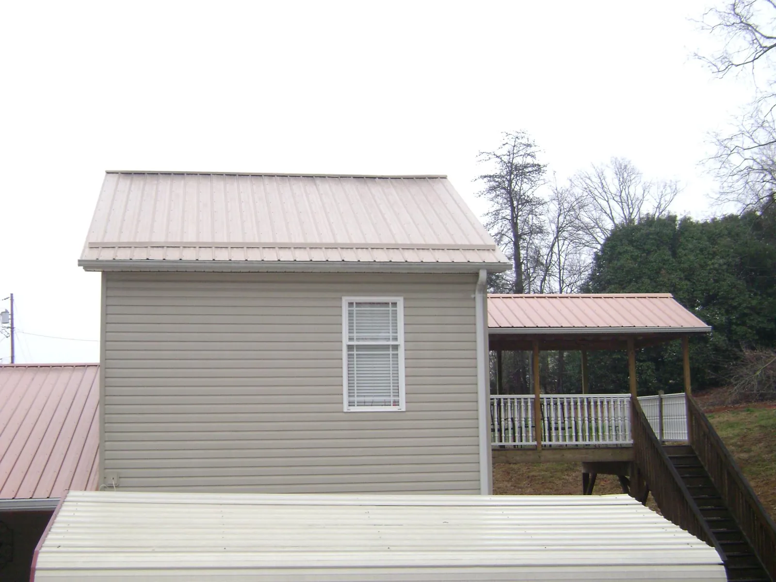 Tan metal roofs on a two story addition and attached porch, from a Roof Replacement job in Murdock